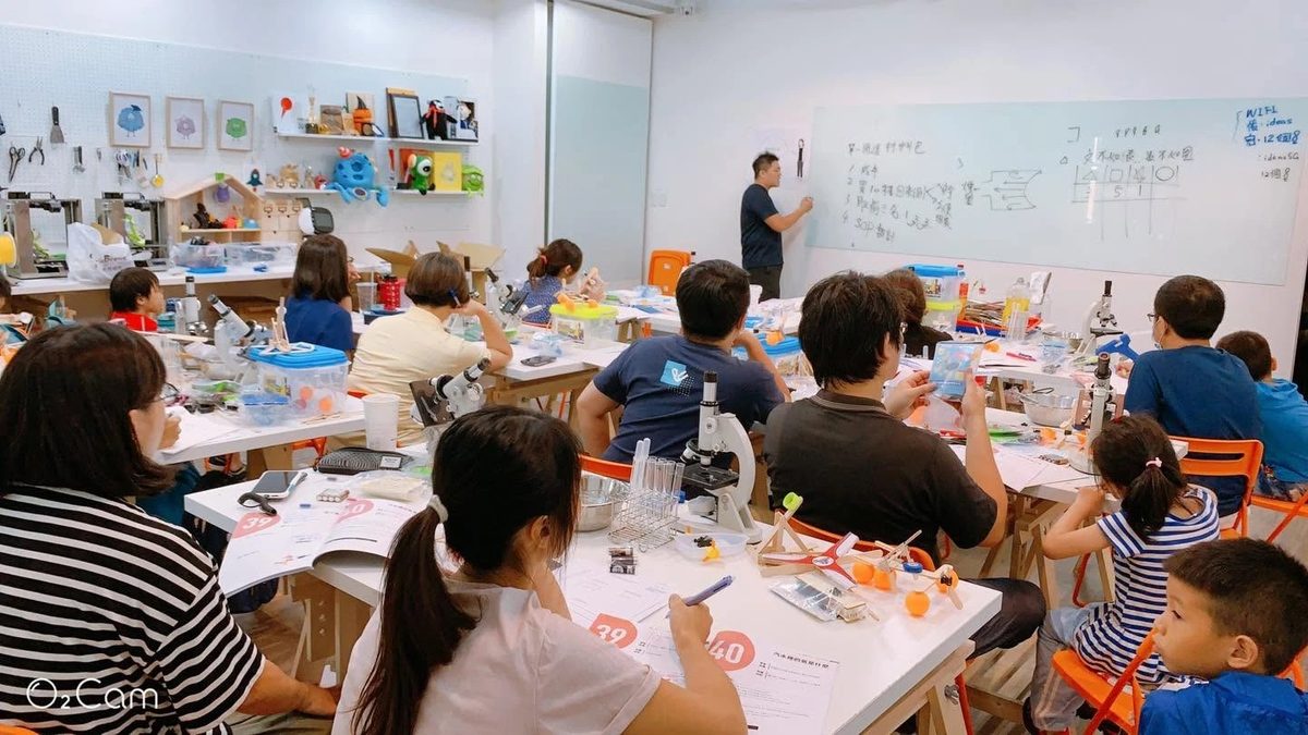 Teacher training session: a room of adult participants each working at their own microscope and apparatus, with the instructor writing the sequence on a whiteboard at the front.