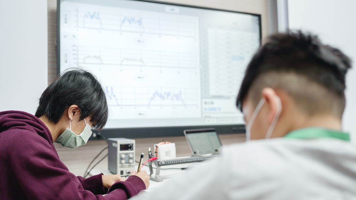 Training session: a tablet in front of a participant shows live data curves, sensors and leads run across the bench, and the course workbook lies open at hand.