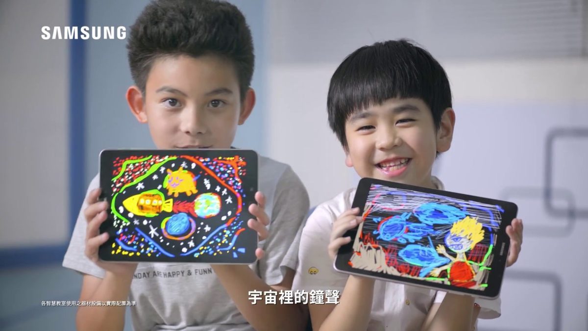 Frame from the commercial: two children laughing as they hold up tablets showing the colourful pictures they drew from sound patterns, with the SAMSUNG logo at top left.