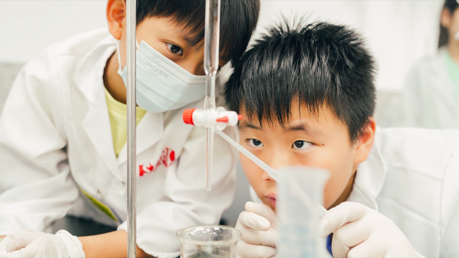 Photograph of a lab bench: a child's hands working with apparatus, beakers and measuring tools on the table.