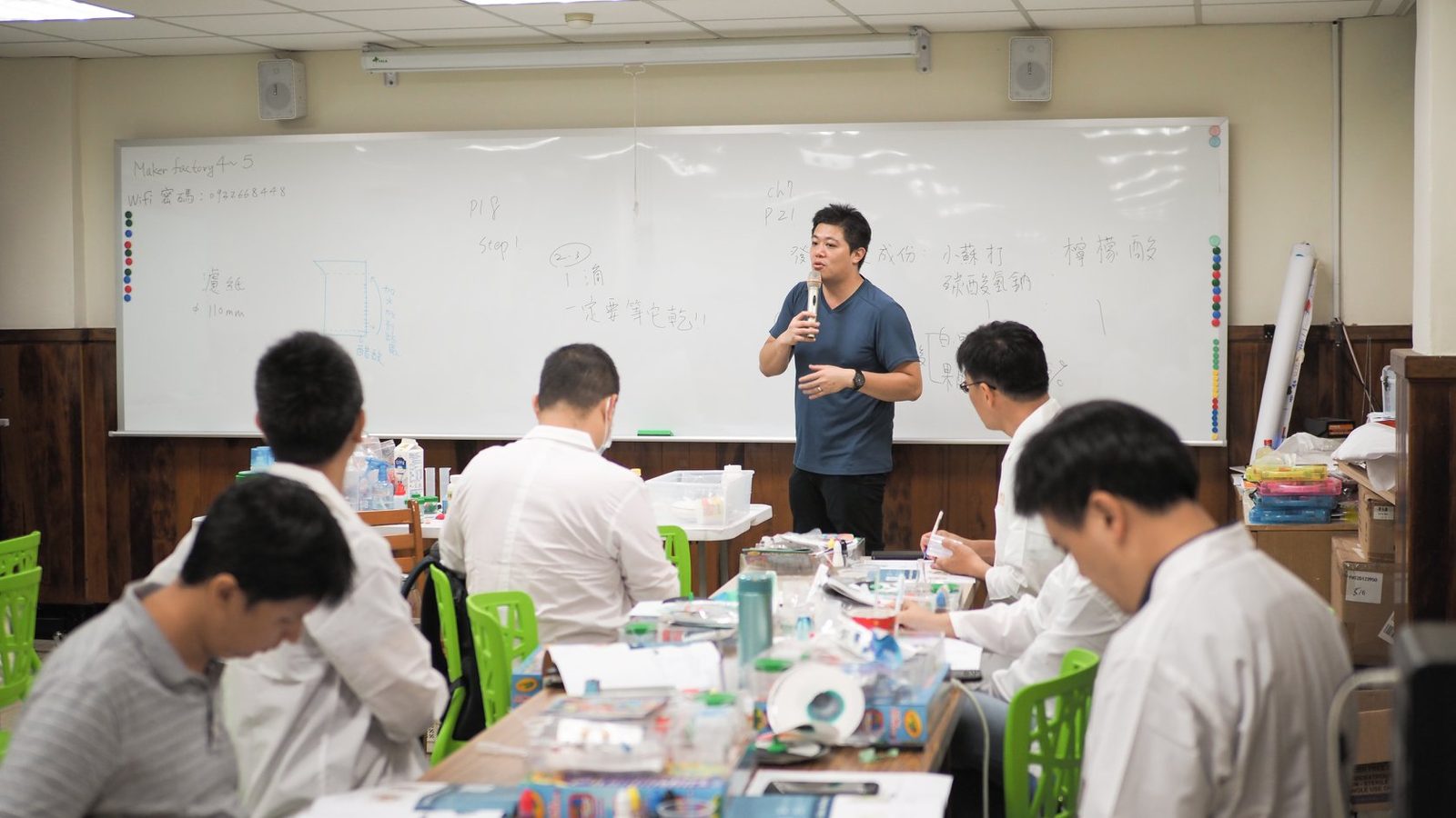 講師於白板前授課，白袍學員滿座
